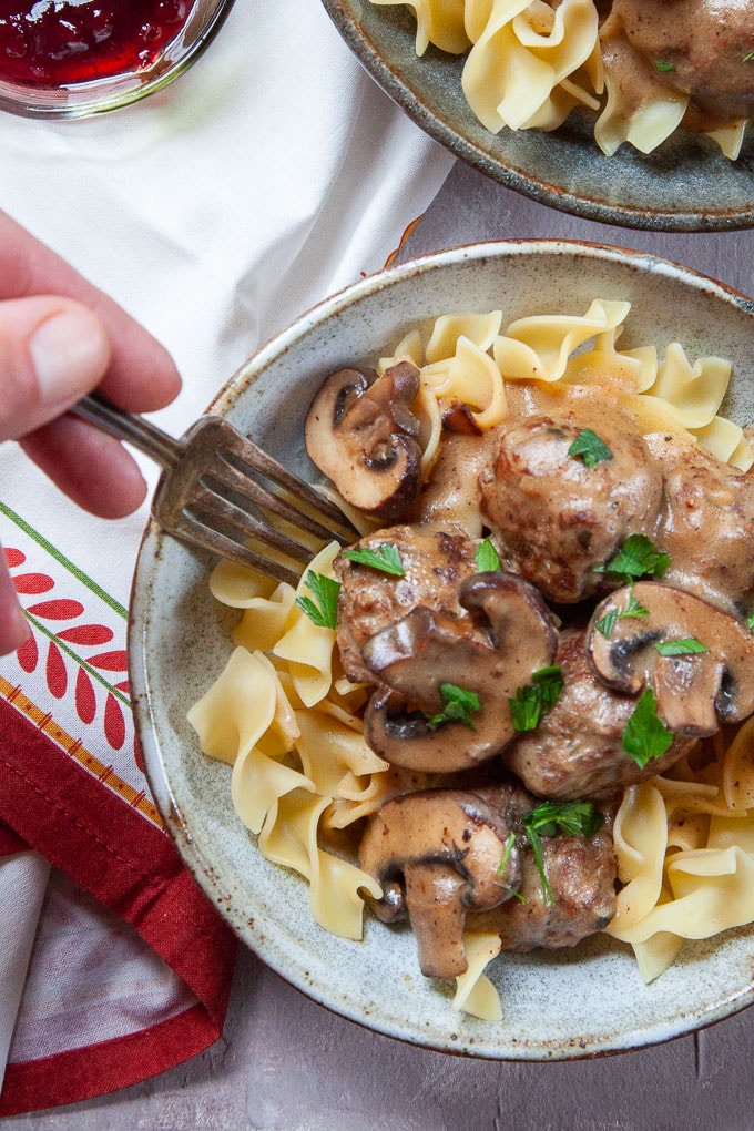 Swedish Meatball Stroganoff, a comforting and savory meatball served in a rich gravy in a bowl with a hand using a fork to reach for a bite.