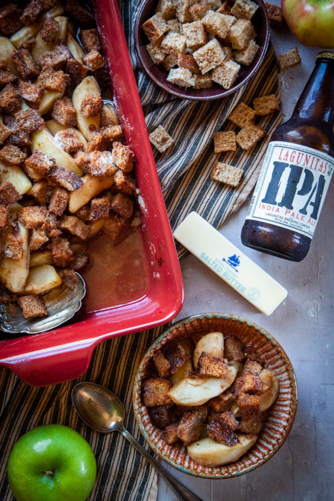 Apple Brown Betty with IPA Beer on a table with ingredients that make up the recipe, including apples, butter, bread cubes and beer.