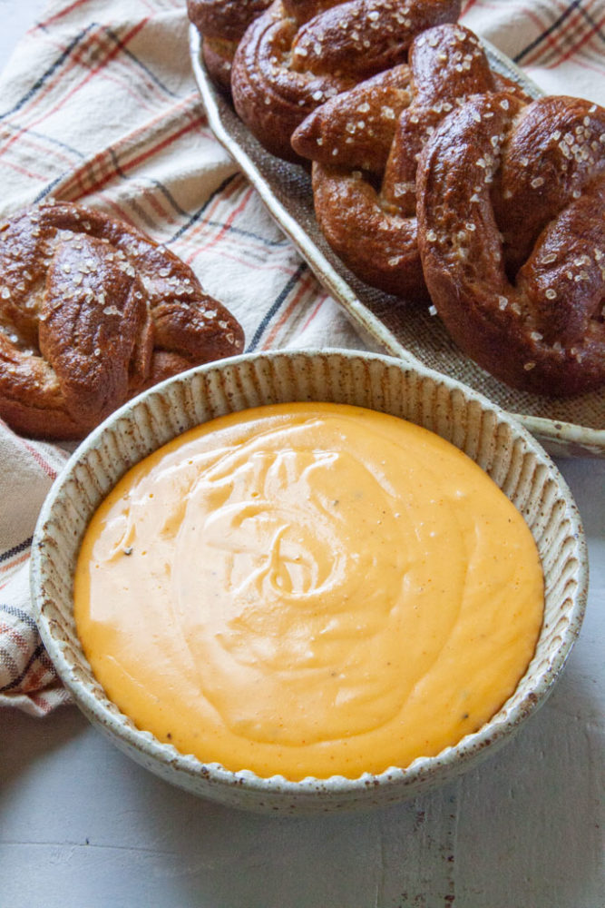 A bowl of easy-to-make beer cheese dip with soft pretzels in the background.