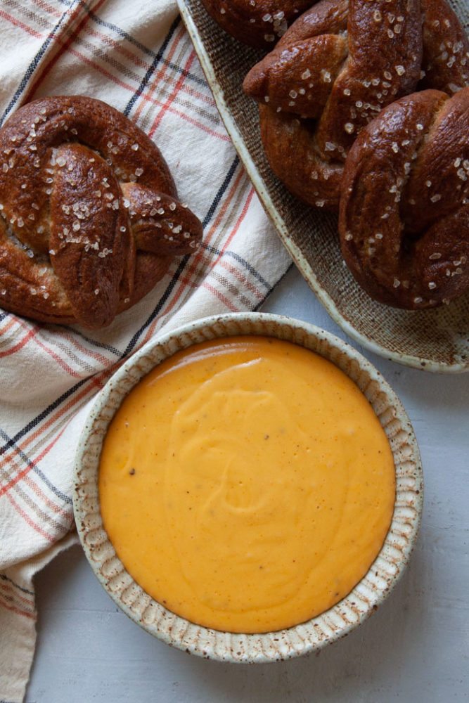 A bowl of beer cheese dip next to a plate of soft pretzels