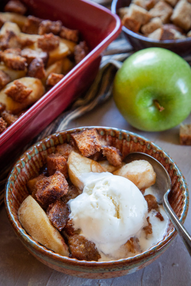 A scoop of vanilla bean ice cream in a bowl of Apple Brown Betty, a traditional rustic American dessert