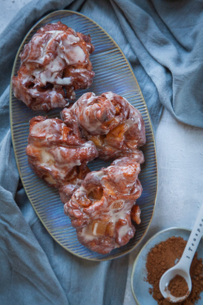 Fried Apple Fritters on a blue plate on a table, with a small plate with cinnamon next to it.