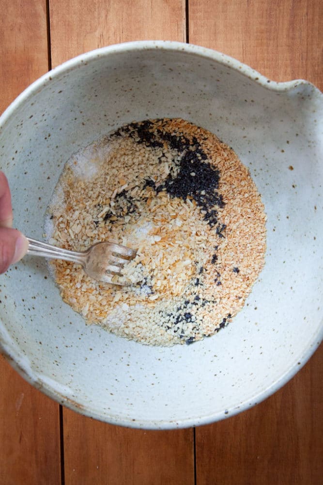 a mixing bowl filled with the components of homemade everything bagel seasoning including dried minced garlic, dried minced onion, poppy seeds, sesame seeds and kosher salt