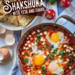 Shakshuka, a thick tomato sauce dish with eggs cooked directly in it, sitting on a table with a bowl of toasted pita on the side.