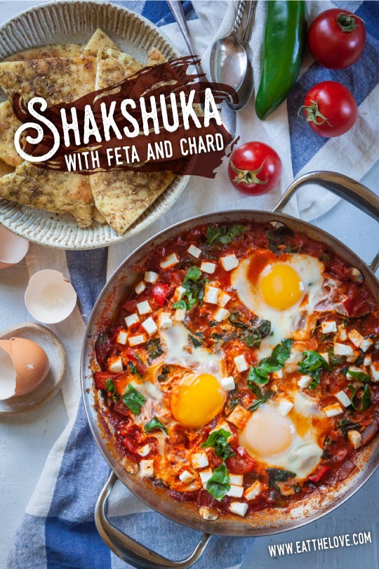 Shakshuka, a thick tomato sauce dish with eggs cooked directly in it, sitting on a table with a bowl of toasted pita on the side.