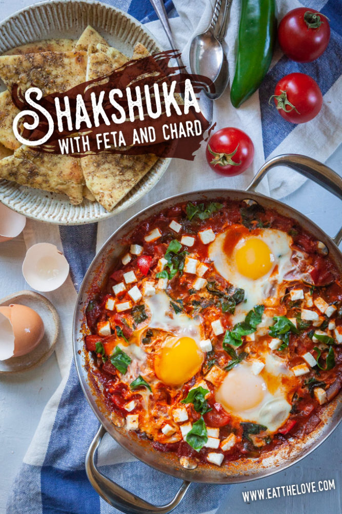 Shakshuka, a thick tomato sauce dish with eggs cooked directly in it, sitting on a table with a bowl of toasted pita on the side.