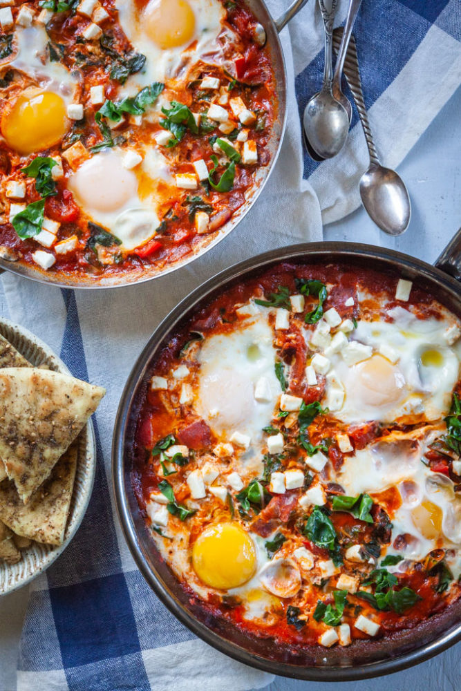 Shakshuka, a thick tomato sauce dish with eggs cooked directly in it, sitting on a table with a bowl of toasted pita on the side.