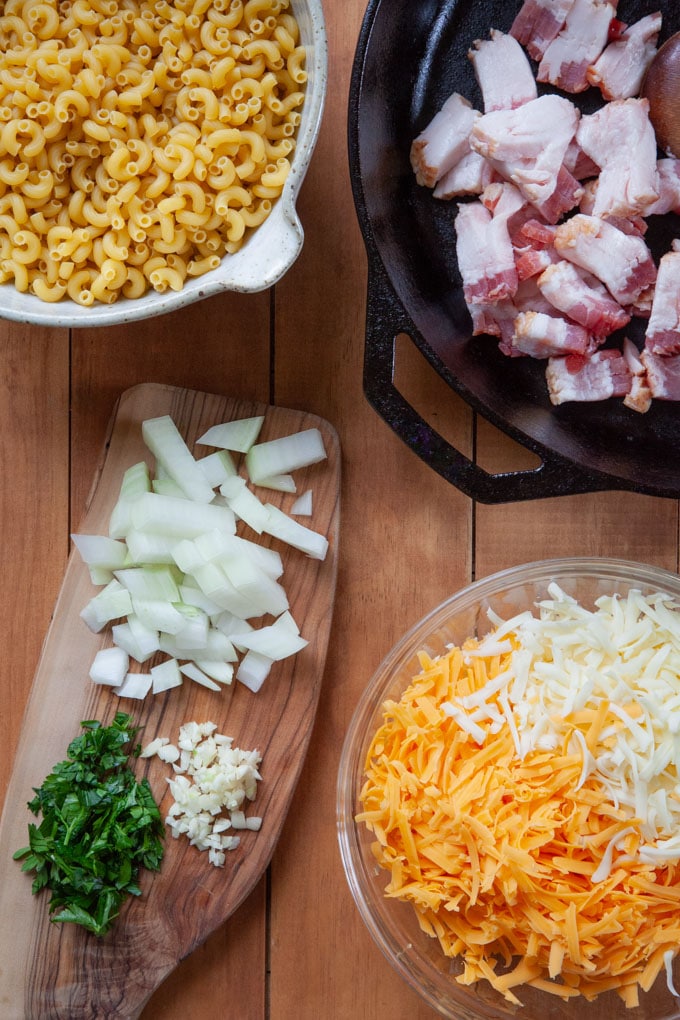 The ingredients for bacon mac and cheese including onions, garlic, chopped parsley, shredded cheese, dry macaroni and bacon!