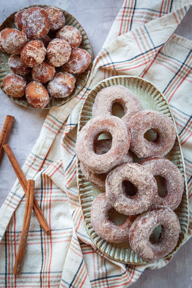 A pile of apple cider donuts on a plate, with a smaller plate of donut holes.