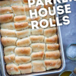Parker House rolls in a pan sitting on a table with melted butter and flaky salt in small bowls next to baking pan.