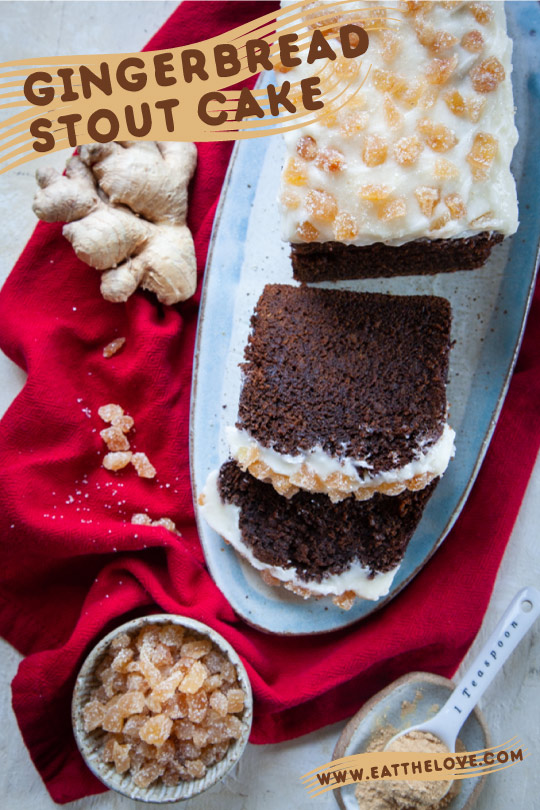 Sliced gingerbread stout cake on a plate surrounded by fresh ginger root, candied ginger, and ground ginger.