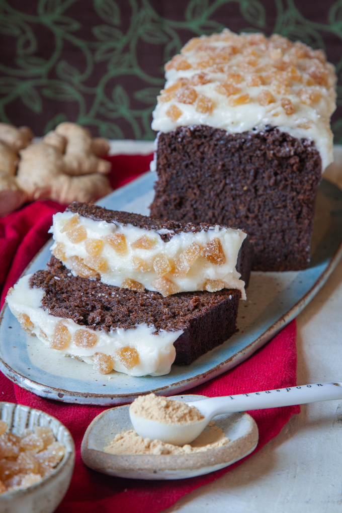 Sliced gingerbread stout cake next to fresh ginger root, candied ginger and ground ginger.