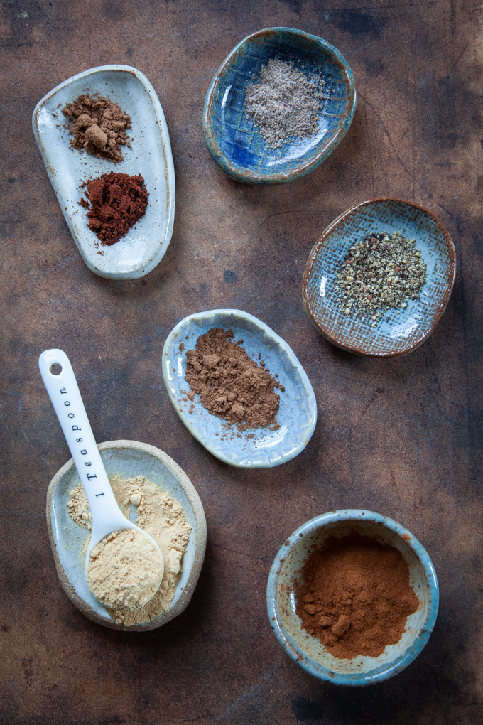 Various warm wintery spices on small dishes, like cinnamon, cardamom, nutmeg, ginger, allspice, cloves, black pepper.