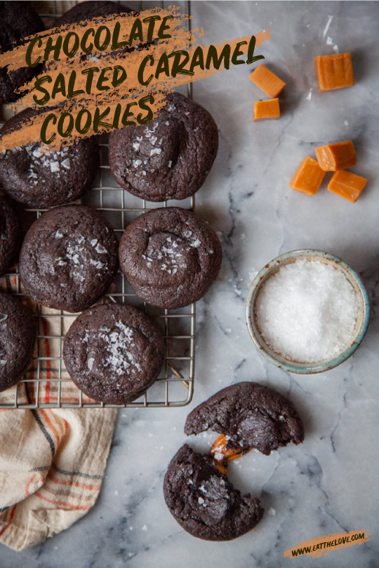 Chocolate salted caramel cookies cooling on a wire rack, with one cookie broken open so you can see the caramel filling on the inside.