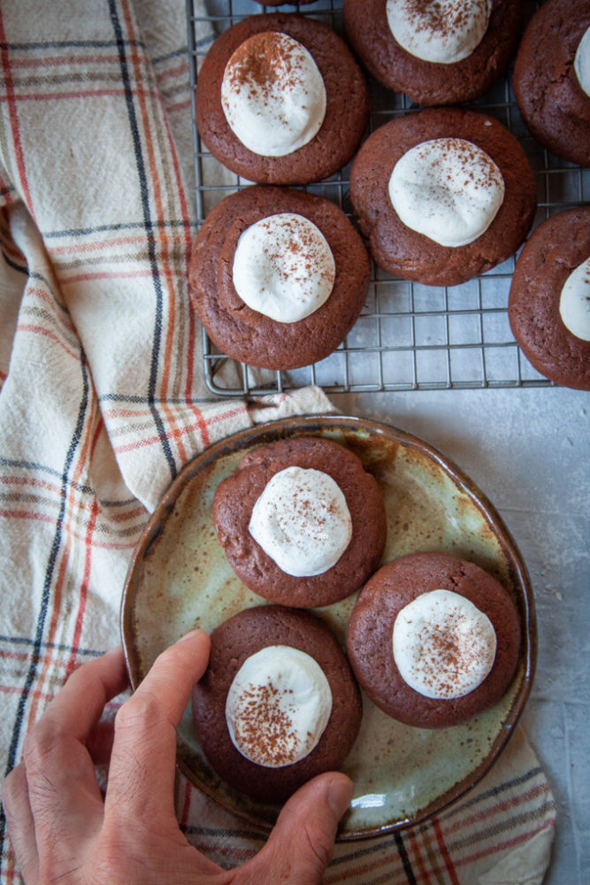 a hand reaching for a hot chocolate cookie on a plate.
