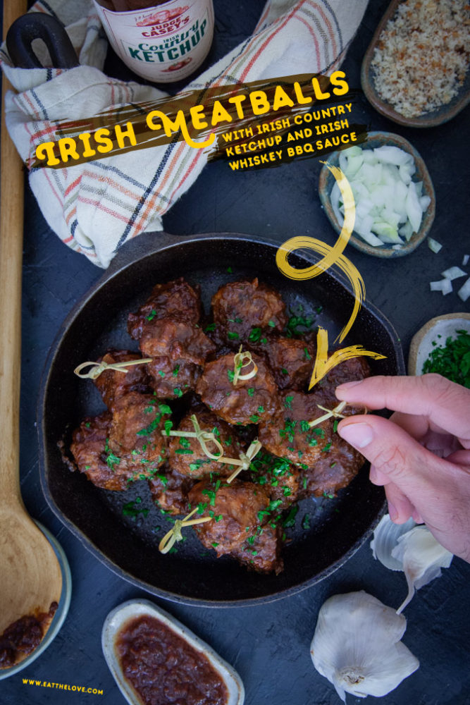 Irish Meatballs in a cast iron skillet, surrounded by some ingredients that are used in the recipe.