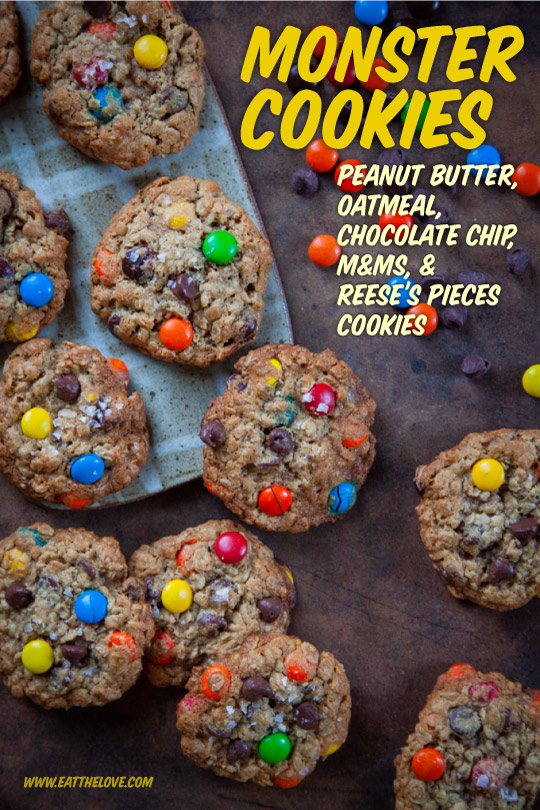 Monster Cookies sitting on a table surrounded by chocolate chips, m&ms and reese's pieces candies.