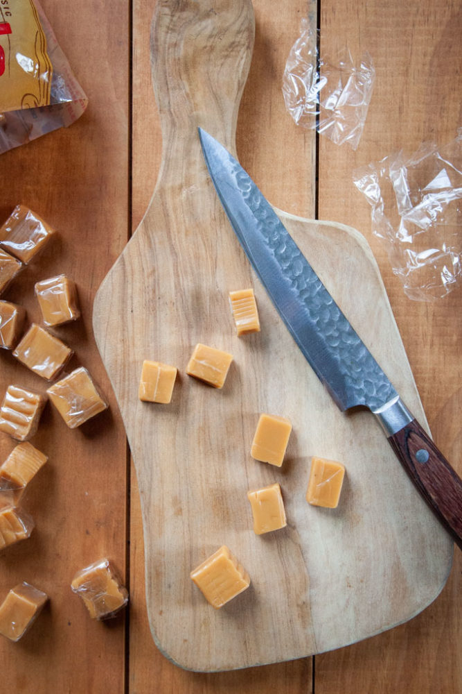 caramel candies cut in half on a cutting board.