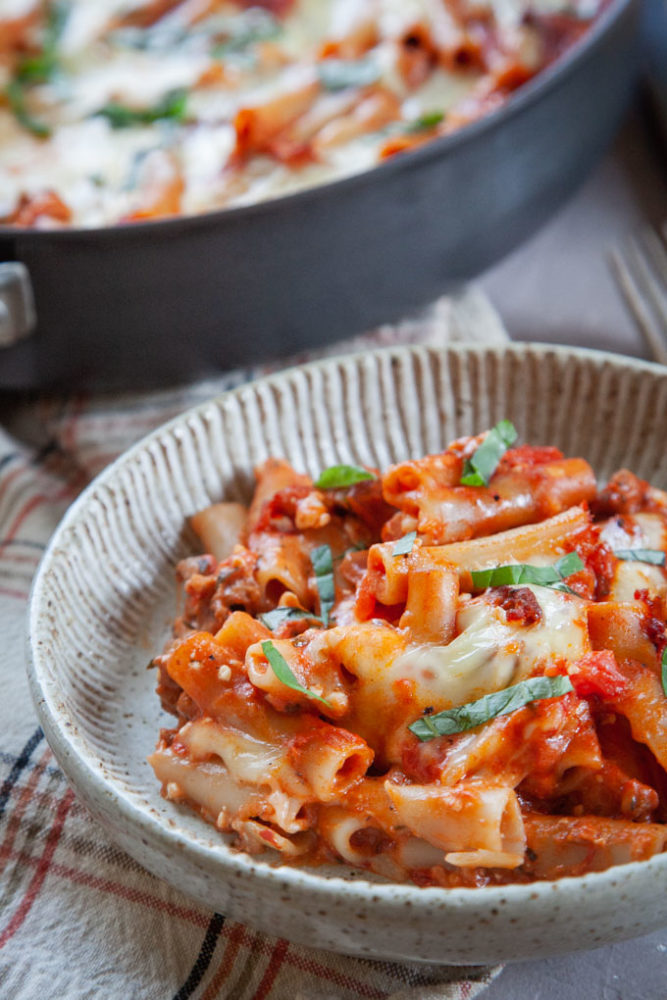 Sausage pasta skillet in a bowl, with the skillet of pasta in the background.