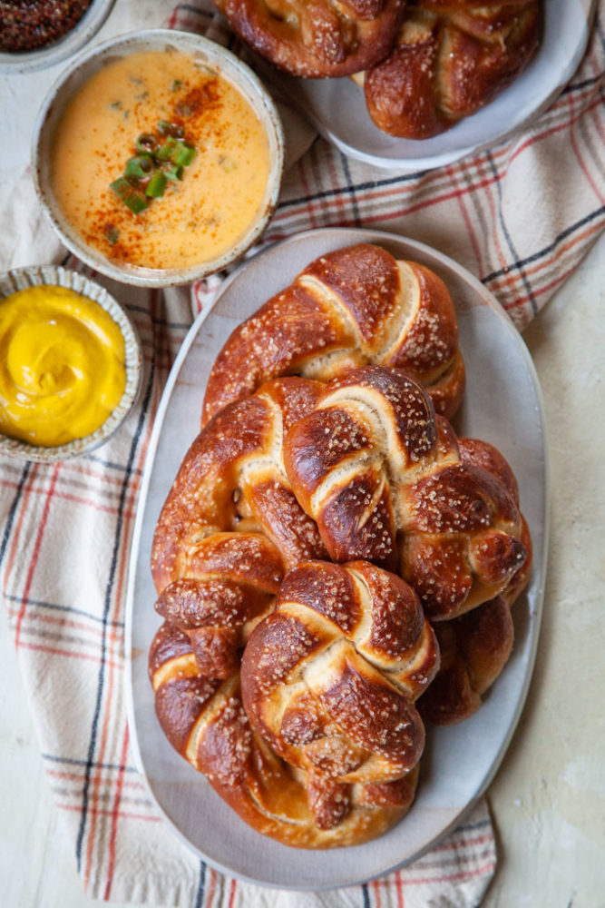 Soft beer pretzels on a plate, with various dips like mustard and beer cheese dip next to the plate.