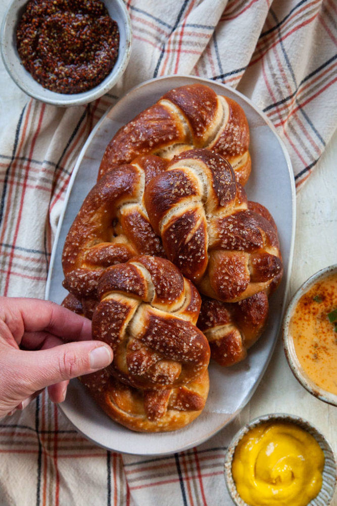 a hand grabbing a soft beer pretzel off a plate.