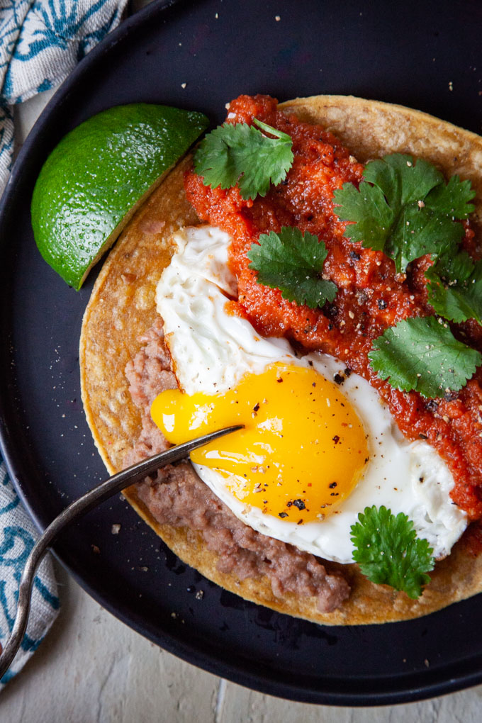 A fork breaking the yolk of an egg on a Huevos Rancheros dish.