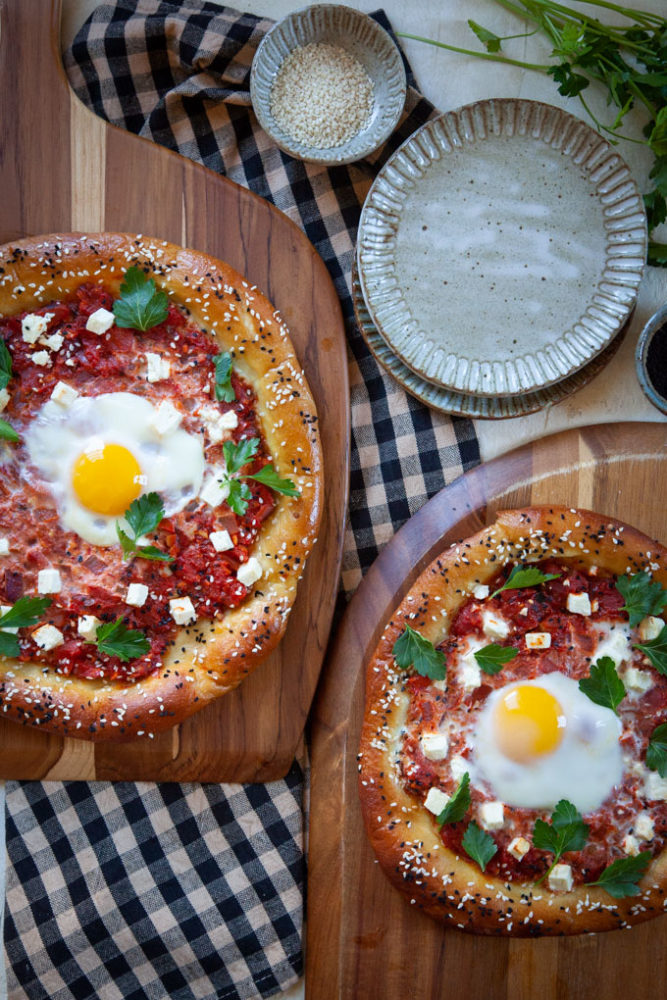 two pretzel shakshuka on a pizza peels next to small plates