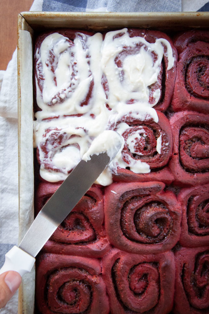Frosting red velvet cinnamon rolls with cream cheese frosting.