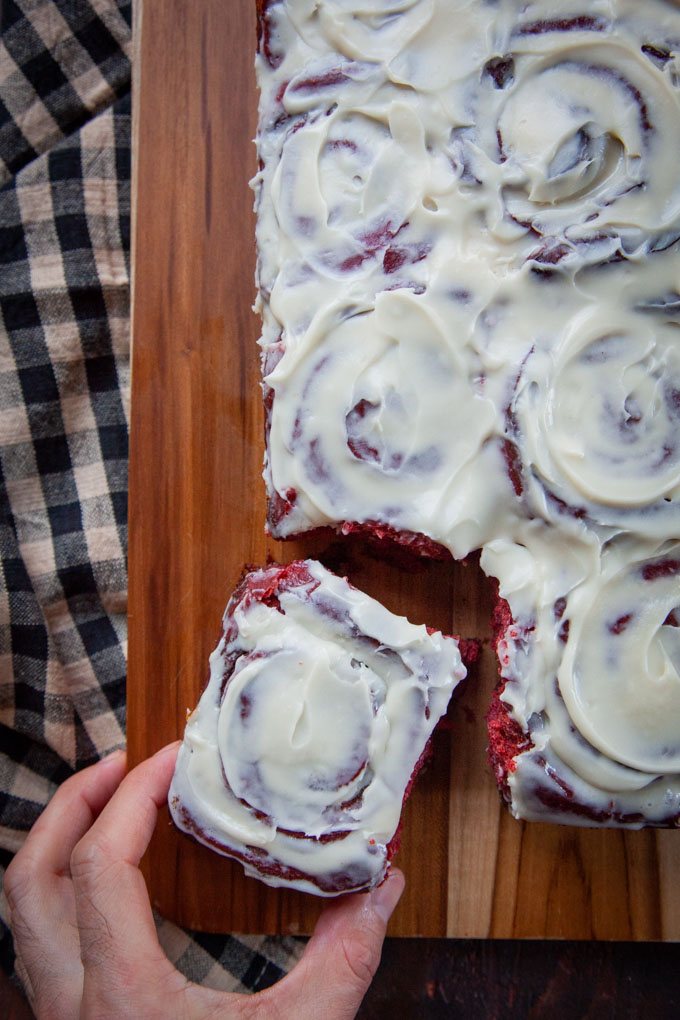 A hand reaching for a red velvet cinnamon bun