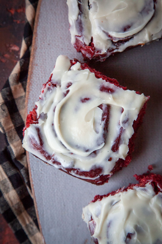 Three red velvet cinnamon rolls on a ceramic cheeseboard.