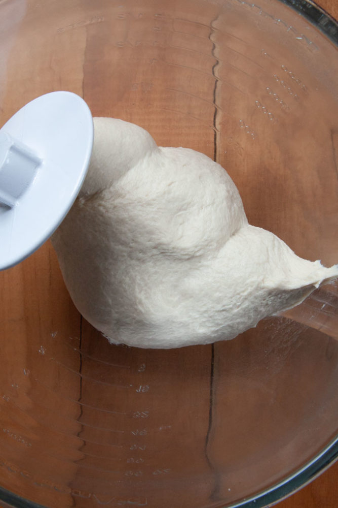 The finished pizza dough on a stand mixer dough hook, looking smooth and elastic.