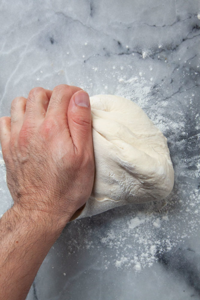 Kneading pizza dough on a marble counter.