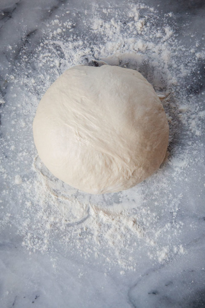 A ball of pizza dough sitting on a marble counter.