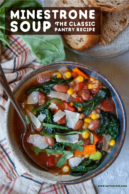 Minestrone soup in a bowl next to some bread and fresh basil.