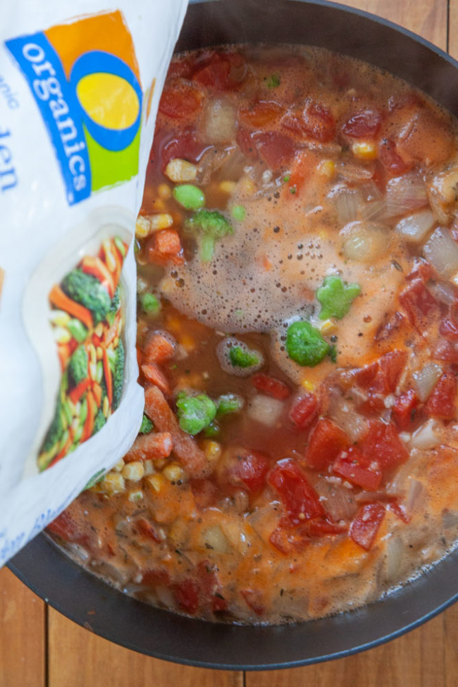 A bag of frozen vegetables being added to a stockpot of minestrone.