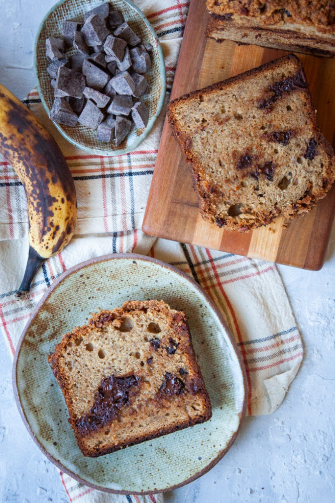 slice of sourdough banana bread on a plate next to the loaf and ingredients.