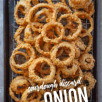 Onion Rings coated with sourdough discard piled up on a sheet pan.