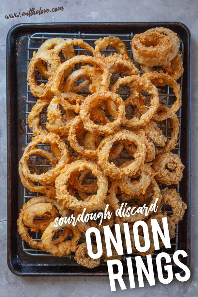 Onion Rings coated with sourdough discard piled up on a sheet pan.