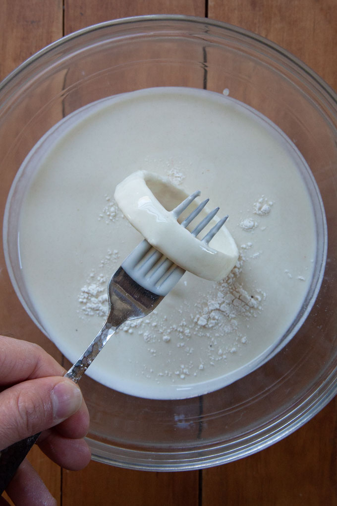 A onion ring on a fork, coated with sourdough starter discard.