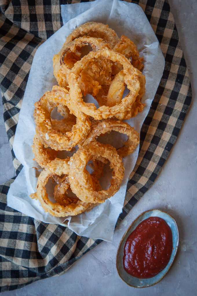 a pile of onion rings on a plate with a small plate of ketchup next to it.