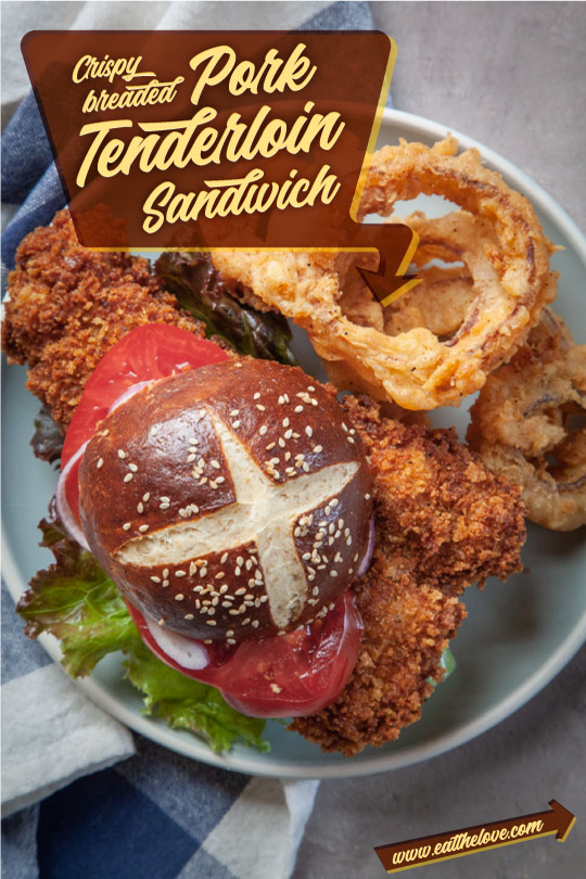 Pork tenderloin sandwich with a pretzel bun on a plate with onion rings.