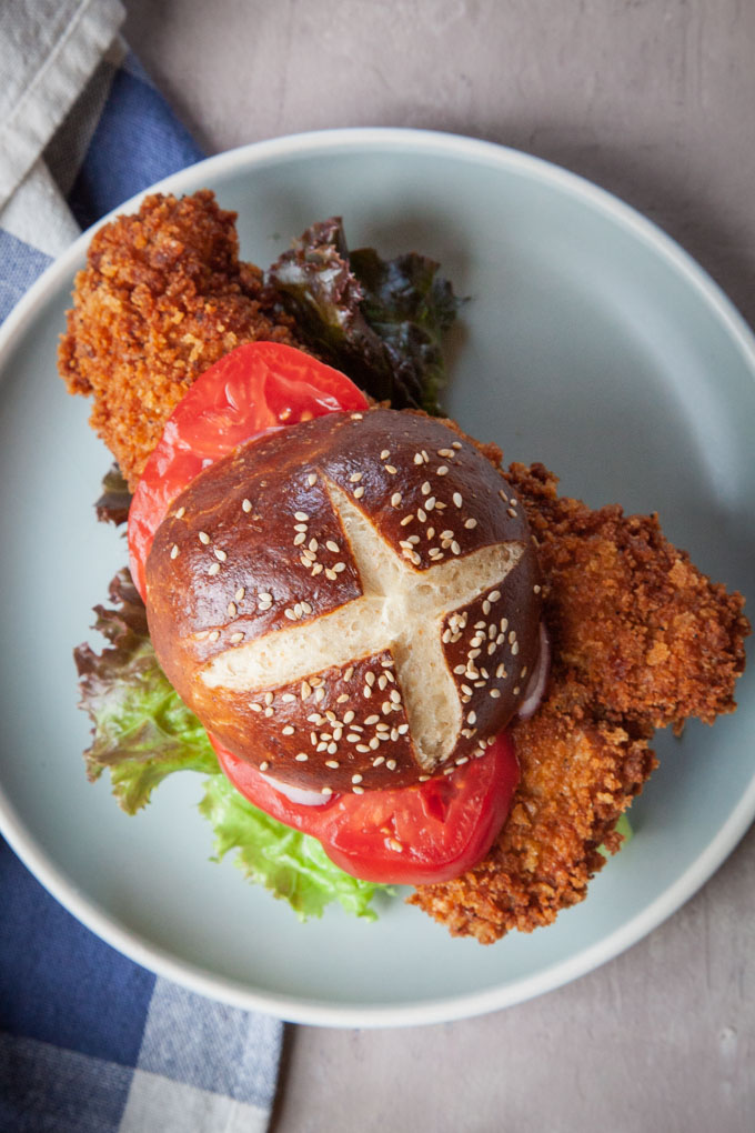 Pork tenderloin sandwich with a pretzel bun on a plate.