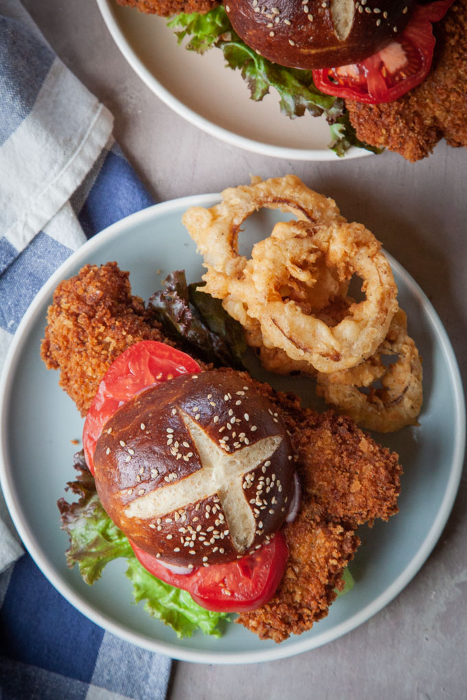 Pork tenderloin sandwich with a pretzel bun on a plate.