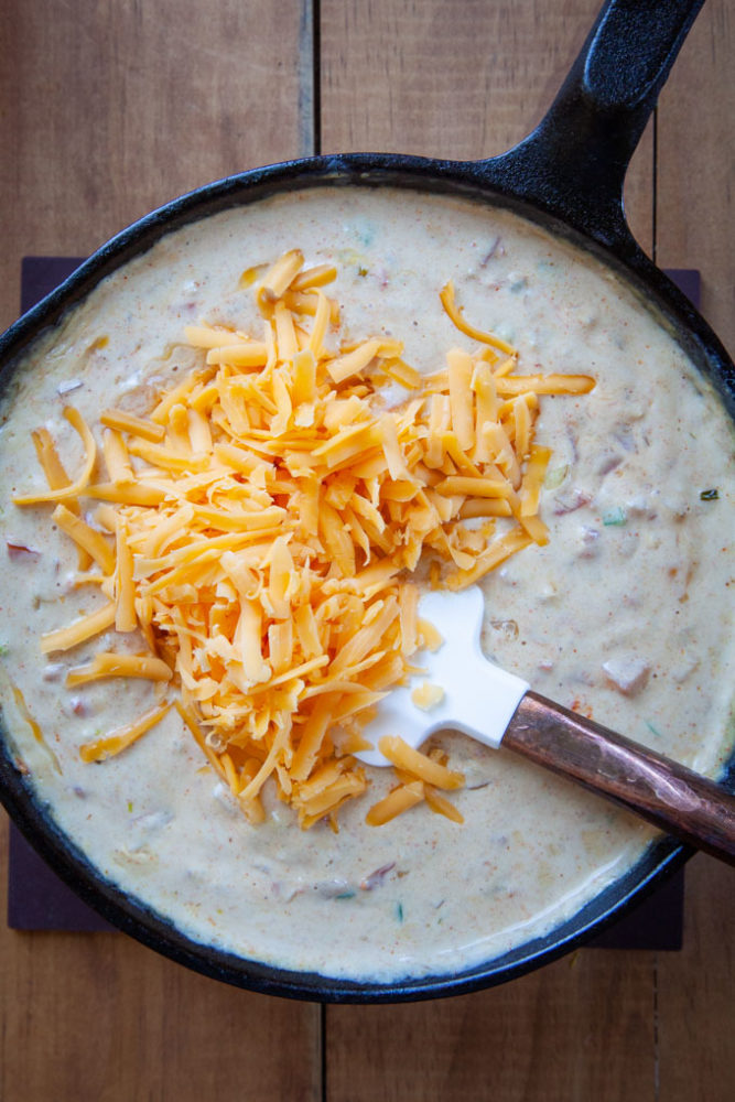 Grated cheese being folded into the queso dip