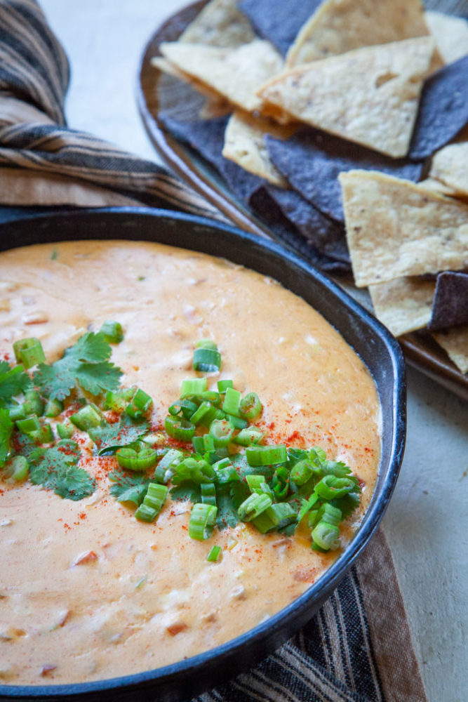 Queso cheese dip in a cast iron skillet next to a plate of tortilla chips.