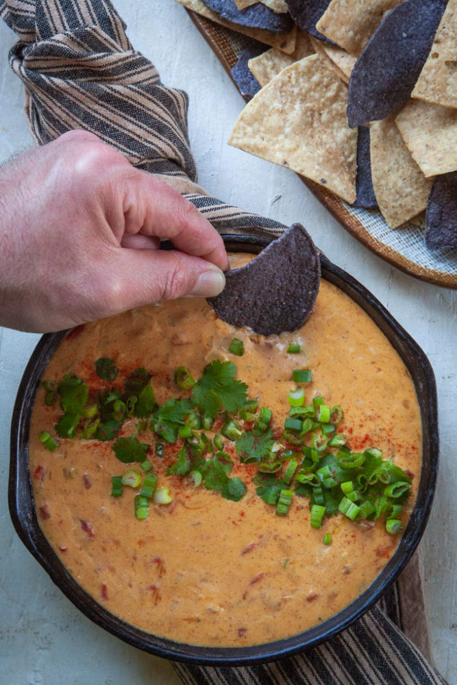 A hand dipping a blue tortilla chip into queso.