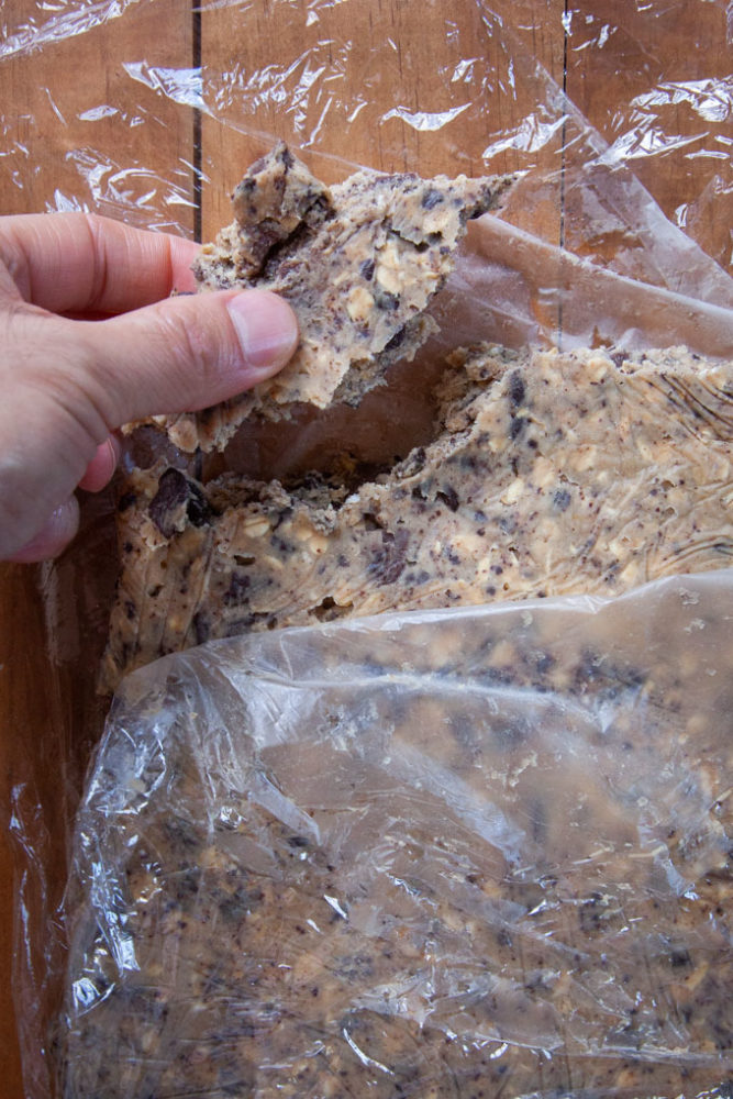 Breaking off a piece of chilled sourdough chocolate chip cookie dough with a hand.