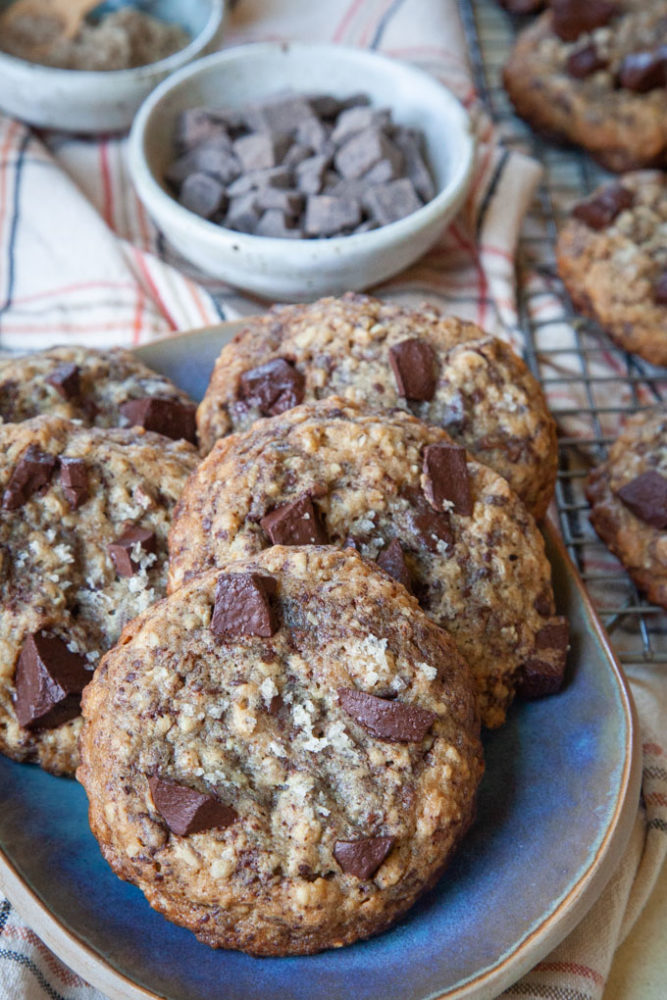 a plate of sourdough chocolate chip cookies with a bowl of chocolate and salt behind it.