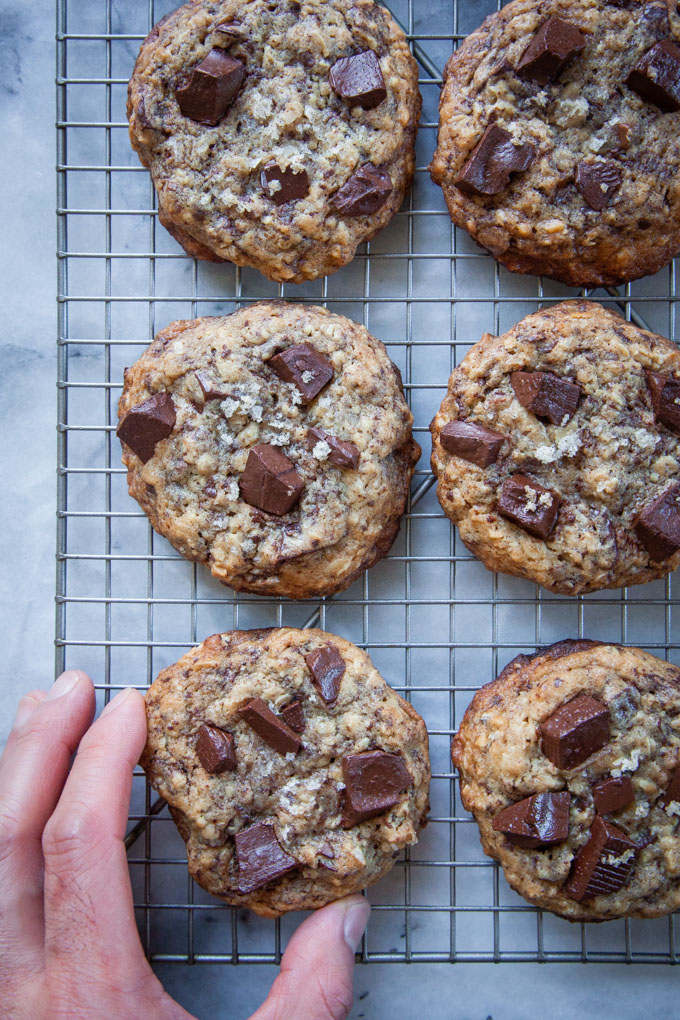 A hand reaching for a cookie on a wire cooling rack.