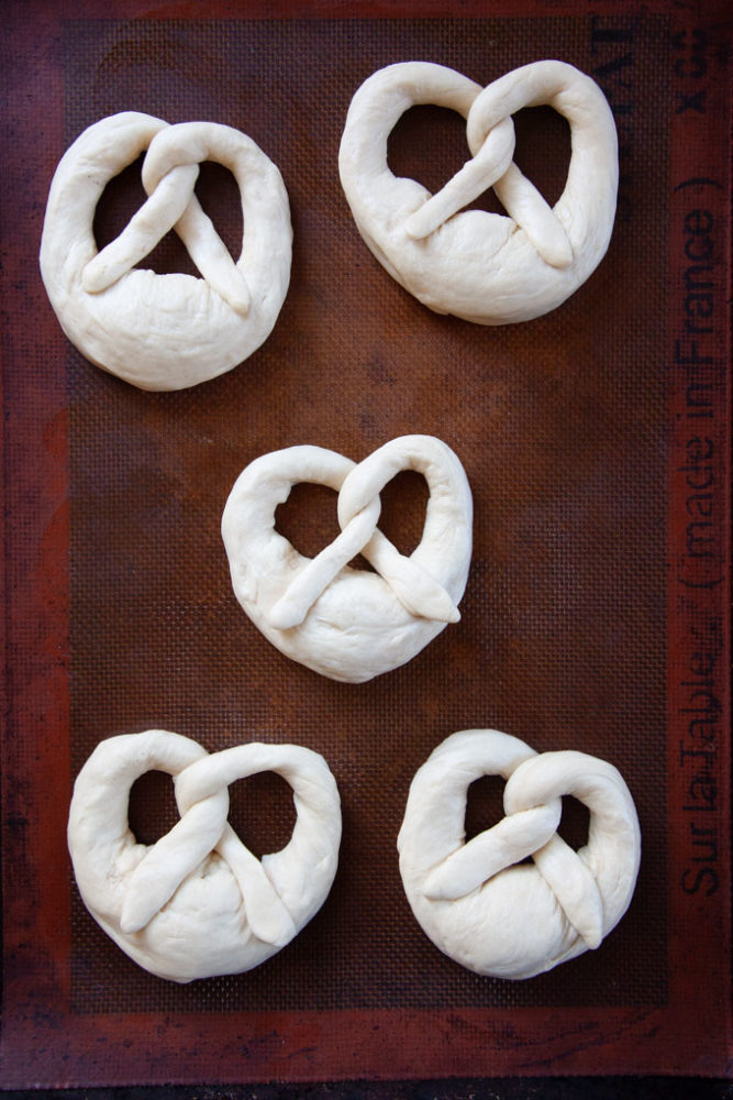 Unbaked sourdough pretzels on a baking sheet.